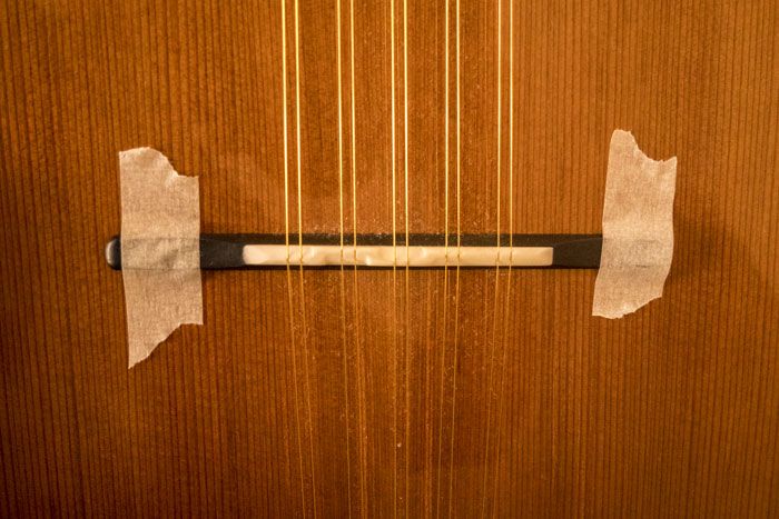 Il ponte della chitarra battente fissato con due strisce di nastro di carta per mascheratura per permettere il cambio delle corde in modo più agevole